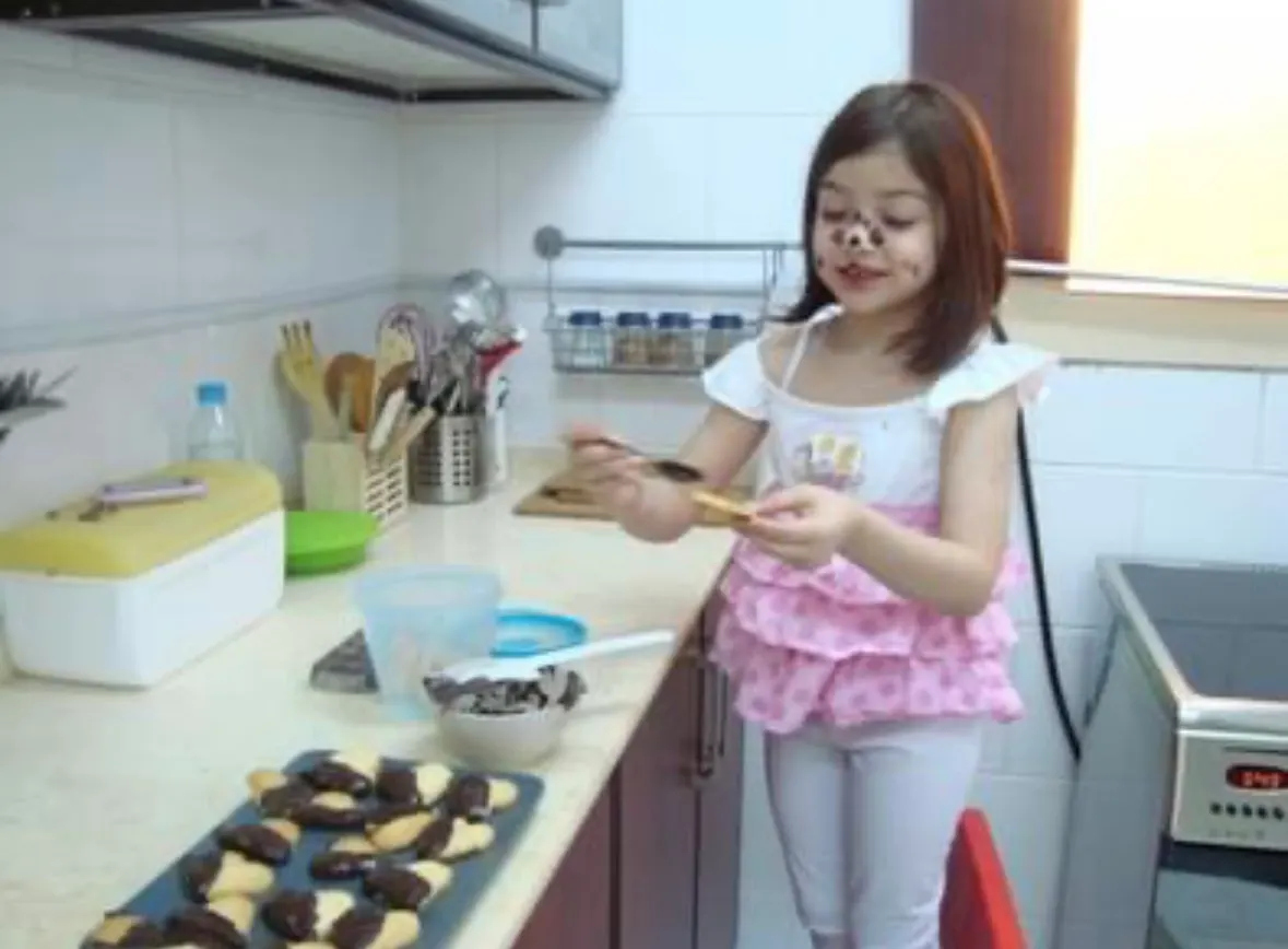 Young Joudi in a kitchen, decorating cookies with chocolate